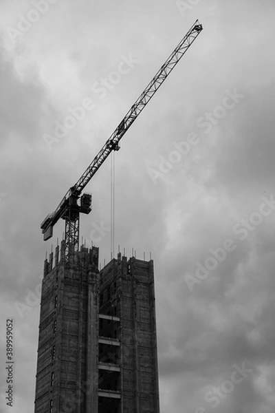 Fototapeta Black and white moody dramatic construction site with crane constructing large tower block