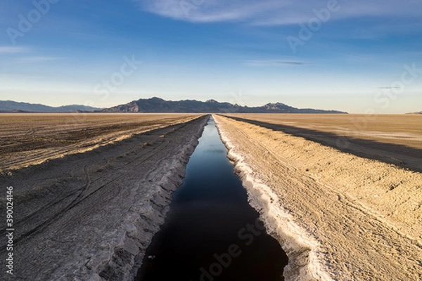 Fototapeta Aerial view of a straight river in the middle of the Bonneville Salt Flats in Utah. Mountains can be seen in the distance and the stream is blue compared with the white of the surrounding salt.
