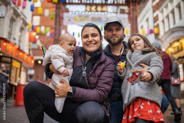 Fototapeta Two happy parents and their two daughters posing in a blurry Chinatown alley
