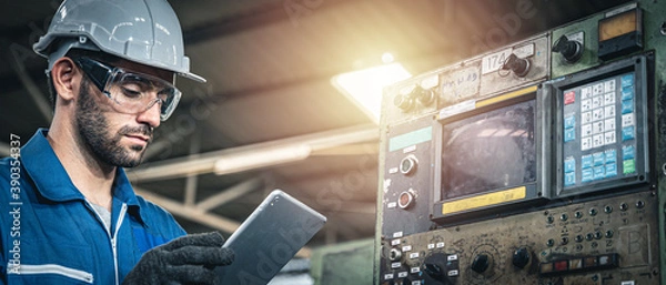 Obraz Male worker in blue jumpsuit and white hardhat inspecting the machine with tablet device.	
