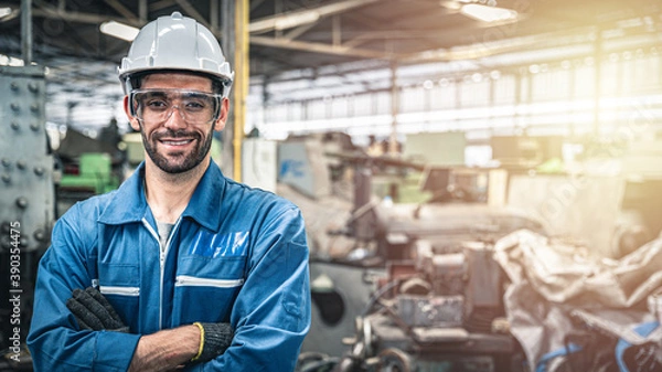 Obraz Pewny siebie inżynier w niebieskim kombinezonie i uśmiechniętym kasku w magazynie.