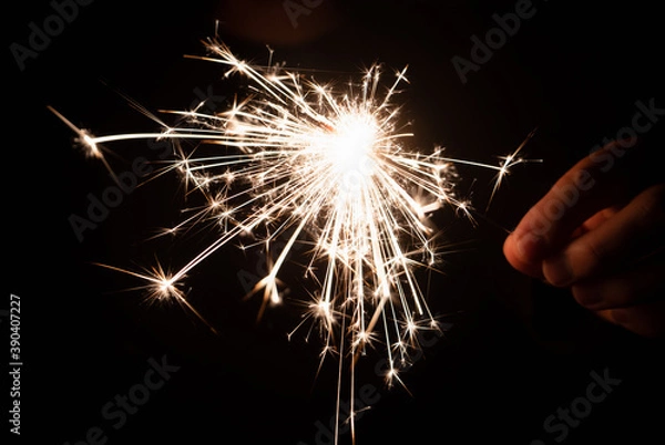 Fototapeta Burning sparkler in hand on a black background. New year, birthday