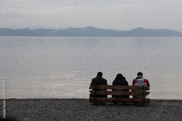 Fototapeta three people are sitting on a bench and looking into the distance against the background of the ocean