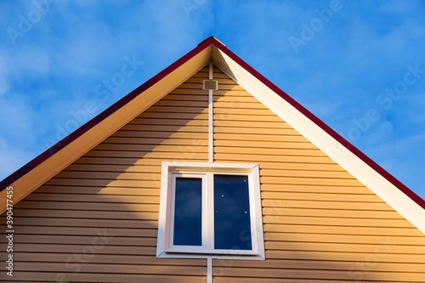 Fototapeta The facade of a new house clad with siding, with windows, against a blue sky, bottom view.
