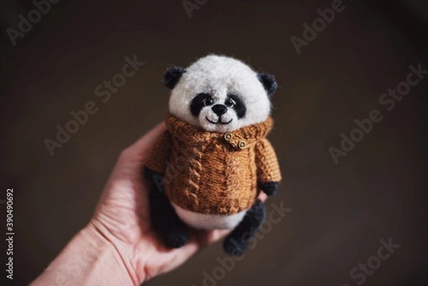 Fototapeta Handmade knitted toy. Amigurumi panda toy in camel color sweater on the wooden  background. Crochet stuffed animals.One of the three sides. front of