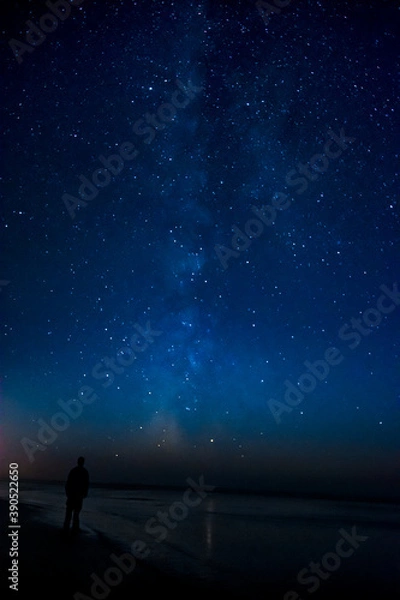 Fototapeta Adventurous man watching the stars on a beach at night. 
