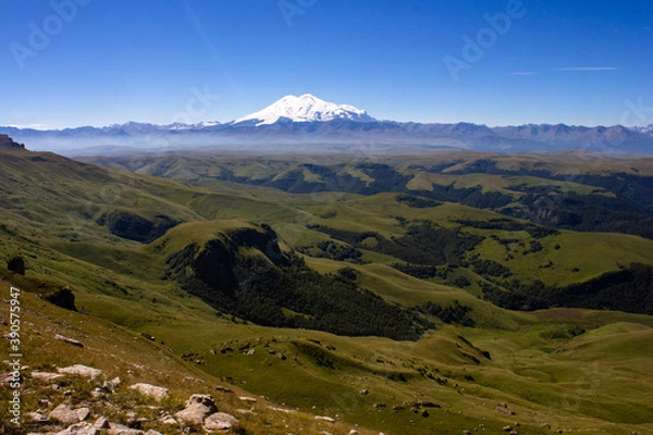 Fototapeta An excellent view from the plateau to the extinct volcano and the snowy peak of Mount Elbrus. Below is a green gorge