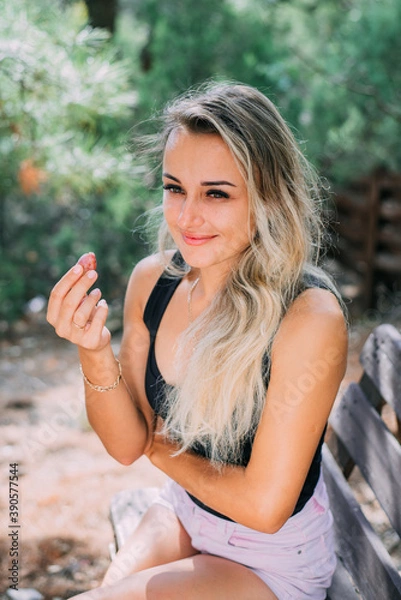 Fototapeta cute girl eats pink grapes sitting on a wooden bench in the woods in the summer in nature