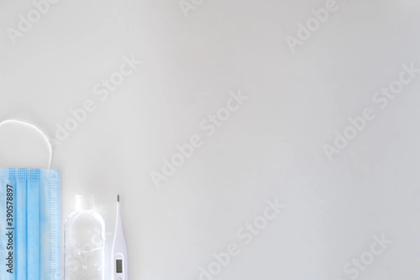 Fototapeta antiseptic in a transparent plastic bottle with a white cap white and white electronic thermometer lie on a light background next to a blue mask
