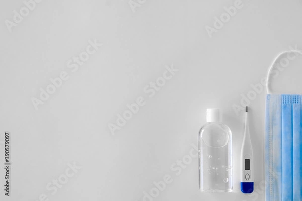 Fototapeta antiseptic in a transparent plastic bottle with a white cap white and white electronic thermometer lie on a light background next to a blue mask