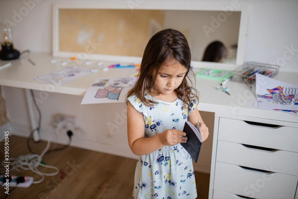 Fototapeta Little girl looking at an American passport with a desk and a mirror behind her