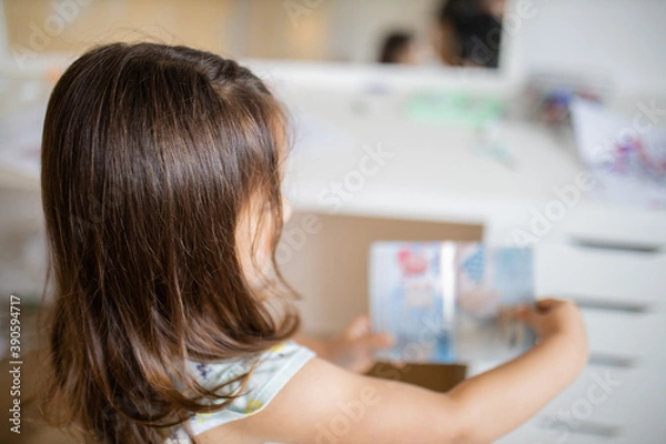 Fototapeta Little girl looking at an American passport in front of a desk and a mirror