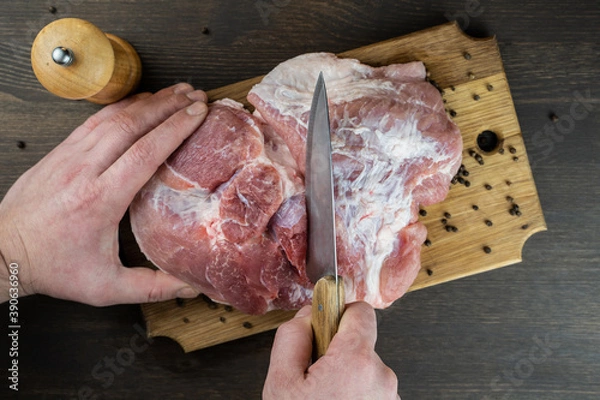 Obraz The cook cuts a juicy raw piece of meat on a wooden Board. The view from the top.