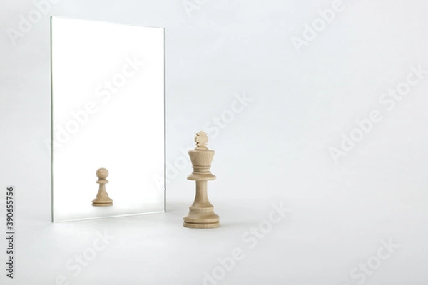 Fototapeta the king is reflected in the mirror as a pawn on white background. underestimation of their abilities