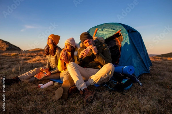 Fototapeta Happy group of friends camping and eating food at the sunset in the mountains.