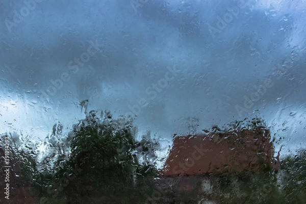 Fototapeta Drops on glass in rainy day.Rain outside window in the countryside. Texture of raindrops, wet glass.Rainy window background.View through the window with stormy sky. Staying at home. Weather changes.