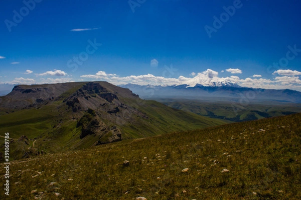 Obraz An excellent view from the plateau to the extinct volcano and the snowy peak of Mount Elbrus. Below is a green gorge