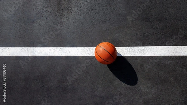 Obraz orange striped basketball ball stands on the white line marking the playing field with asphalt tarmac, sports object lit by sun light on playground top view with copy space, nobody.