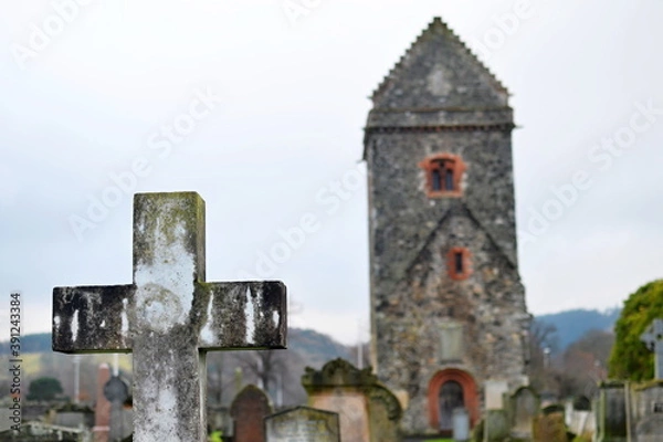 Fototapeta Old cemetery cross with a stone church tower in the background
