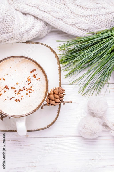 Fototapeta Cappuccino with cinnamon, a branch of a pine tree and knitted accessories on a white wooden background