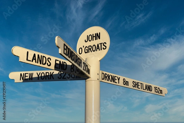 Fototapeta New John O'Groats signpost on NC500 route with blue sky and light cloud background. Mileage to Orkney, Shetland, Lands End, Edinburgh and New York. Famous spot for tourists to get photographs taken.