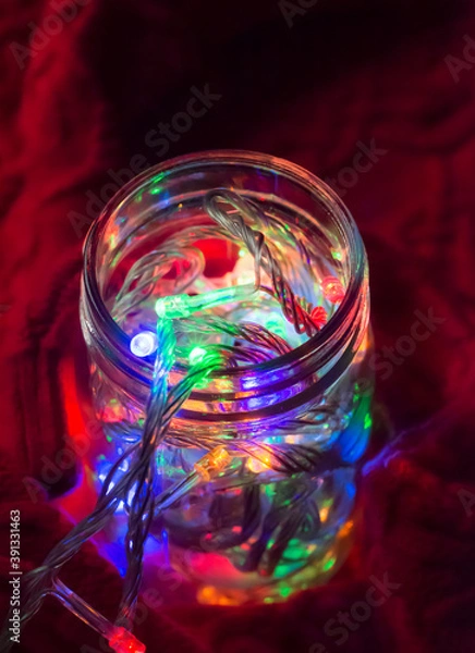 Obraz Lights inside the glass jar on a red sweater, colorful light glowing in the dark inside the jar.