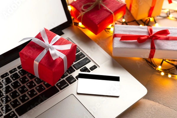 Fototapeta Gifts and credit card on the laptop with blurred bokeh lights. Christmas online shopping, sales and discounts promotions during the Christmas holidays, online shopping at home and lockdown coronavirus