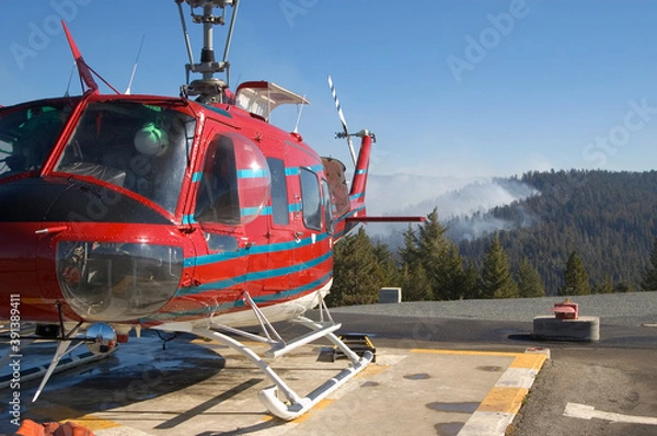 Obraz Fire fighting helicopter refueling, smoke in background.