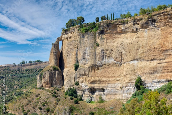 Fototapeta Summer view of the high rock face of the Andalusian city of Ronda in sunshine and a blue sky with clouds. The rock on the left looks like a tower.
