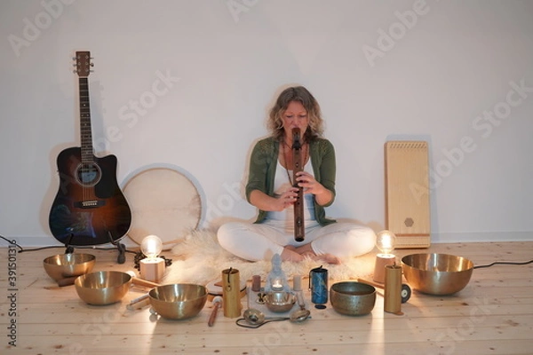 Fototapeta Woman sitting with a native Indian flute for a sound healing session with many sound healing instruments in front of her like singing bowls, koshi chimes, drum, sansula and zimbel.