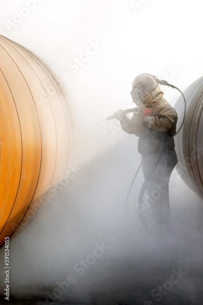 Fototapeta Ręczne piaskowanie lub piaskowanie rur metalowych. Obróbka strumieniowo-ścierna, bardziej znana jako piaskowanie, to operacja polegająca na wymuszonym wbijaniu strumienia materiału ściernego w powierzchnię.