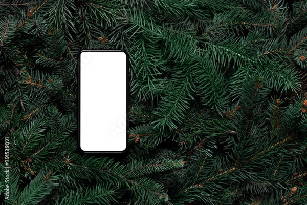 Fototapeta Mock up. Smart phone on Christmas tree branches. Top view, flat lay, copy space. Nature New Year holiday concept. Pine, fir pattern. Christmas shopping online. Mobile app