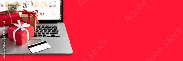 Fototapeta Christmas shopping online concept. Laptop with red gifts and credit card on the red background. Banner, copy space, mock up. Holiday winter sales, discounts, e-commerce