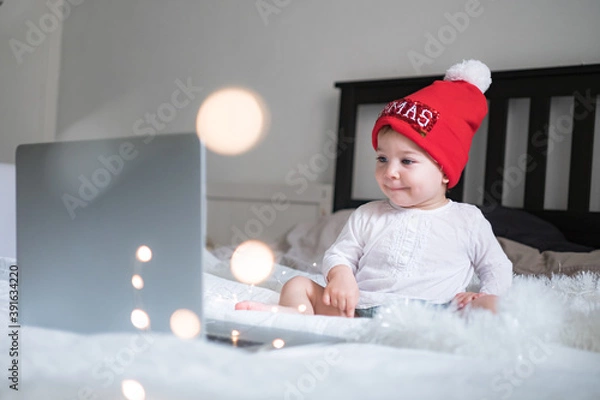 Obraz Infant baby in Christmas hat chatting via lap top at home during quarantine. Social distancing during lock down. New year and Christmas celebration at home