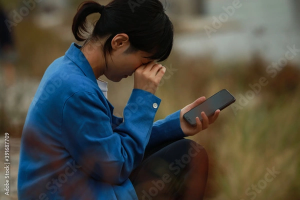 Fototapeta スマートフォンを手に持ち泣く女性