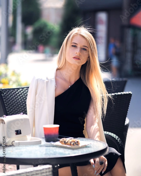 Fototapeta Girl posing at a table in a cafe in the city in a sexy black dress
