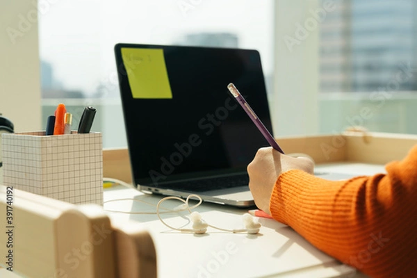 Fototapeta Student taking note with pencil on a book. Study and learn from home at working desk laptop.