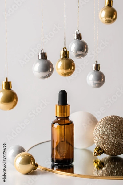 Obraz Christmas minimalistic composition with brown glass serum bottle on the mirror and hanging golden balls. Health and beauty concept.