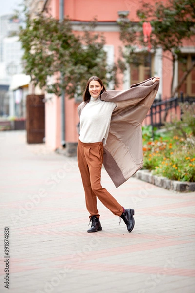 Obraz beautiful long-haired brunette in a light beige coat on the streets of the old city