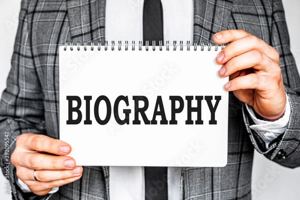 Fototapeta business, technology, internet and networking concept - businessman in gray fashionable business suit holding a white notebook with conference inscription BIOGRAPHY inscription