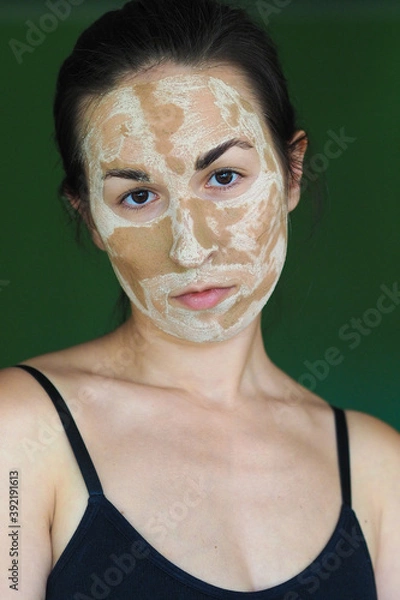 Obraz young brunette woman with a clay homemade mask on her face looks into the frame