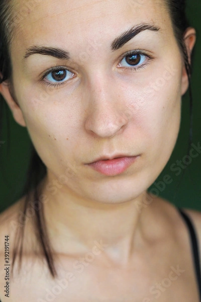 Obraz close-up of a young brunette woman looking at the camera on a green background