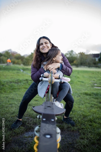 Fototapeta Joyful mother and little daughter smiling while playing on a seesaw