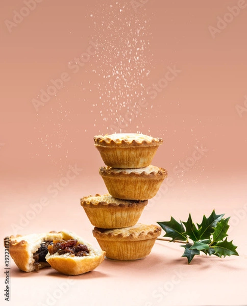 Fototapeta Mince pies stacked on each other on pink background with sugar sifting on top. A mince pie is a traditional Christmas sweet pie, filled with a mixture of dried fruits and spices.