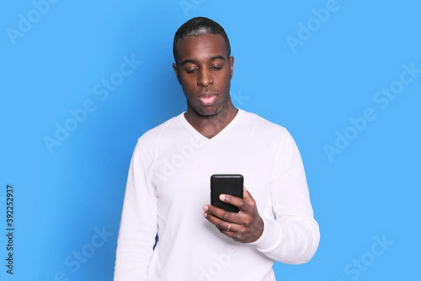 Fototapeta Cheerful African American man in white sweater using mobile phone application.