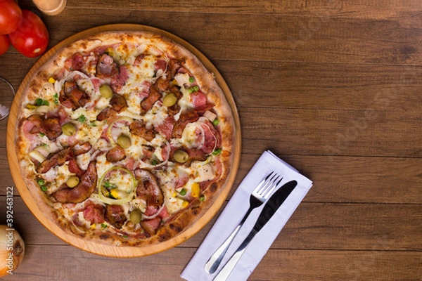 Fototapeta Tasty Portuguese Pizza made with ham, pea egg, heart of palm, pepperoni, onion and mozzarella and bacon. Served on wooden board. Top close-up photograph. Space for texts and graphic arts.