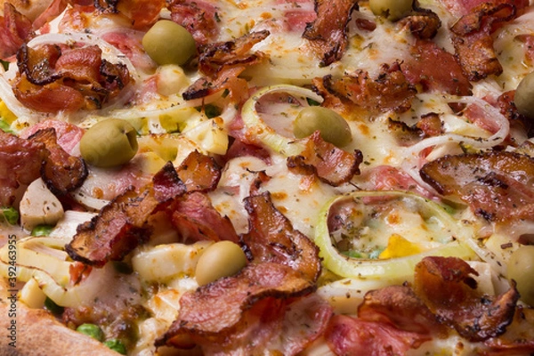 Obraz Tasty Portuguese Pizza made with ham, pea egg, heart of palm, pepperoni, onion and mozzarella and bacon. Close-up photograph of the pizza filling. Restaurant. and Pizzeria.
