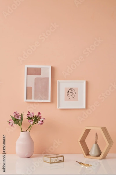 Fototapeta Two pictures in frames on pink wall by table with flowers in white ceramic vases