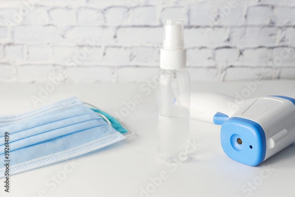 Obraz Surgical masks, thermometer and hand sanitizer on white background 