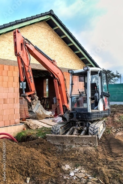 Fototapeta Mini excavator on construction site. Construction of a family house. Construction of a water supply network. Construction site with a small excavator.